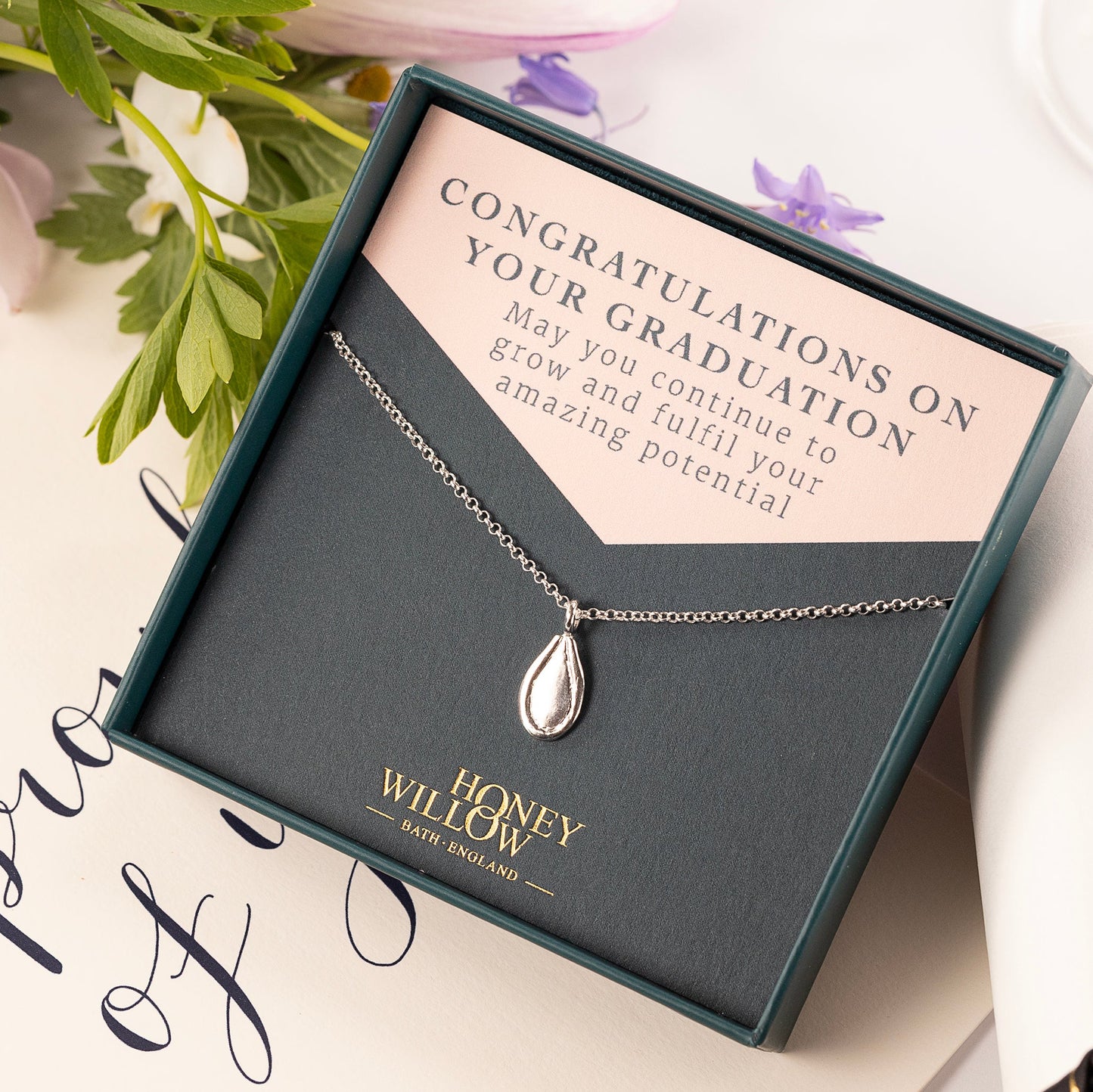 Necklace in a gift box with a graduation card and flowers on a white background