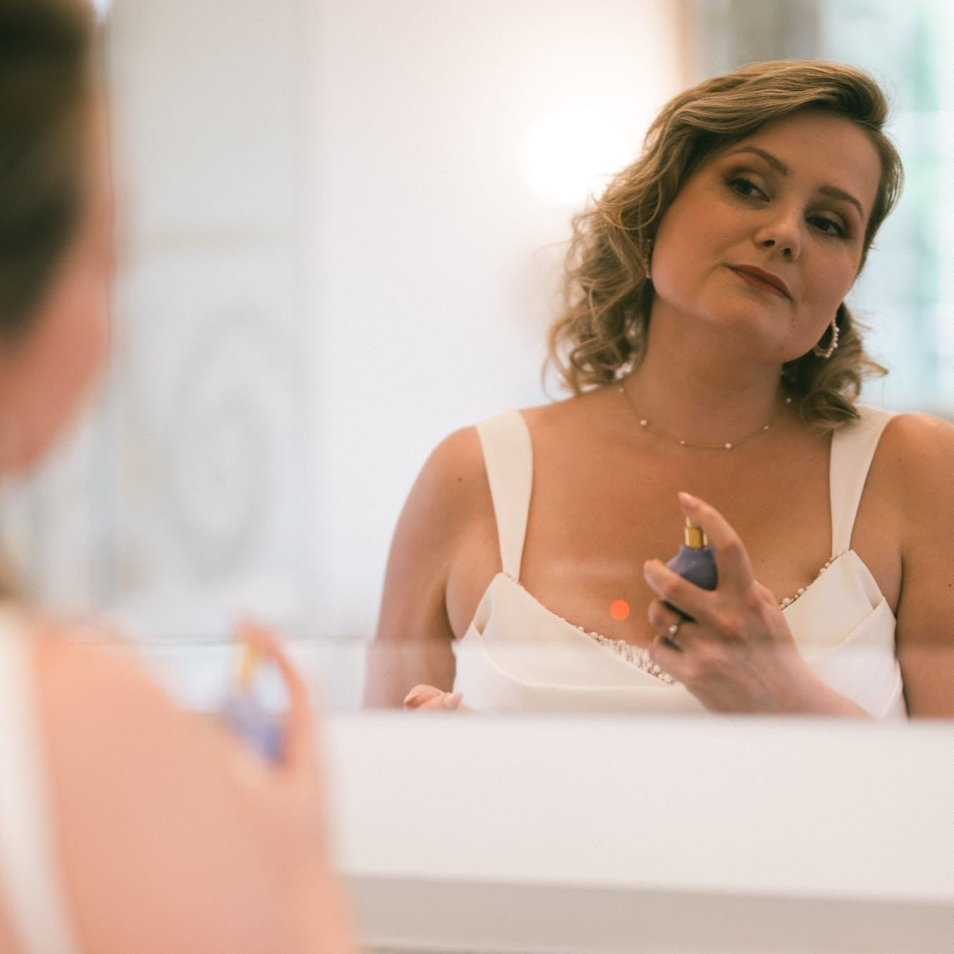 Woman applying perfume in front of a mirror