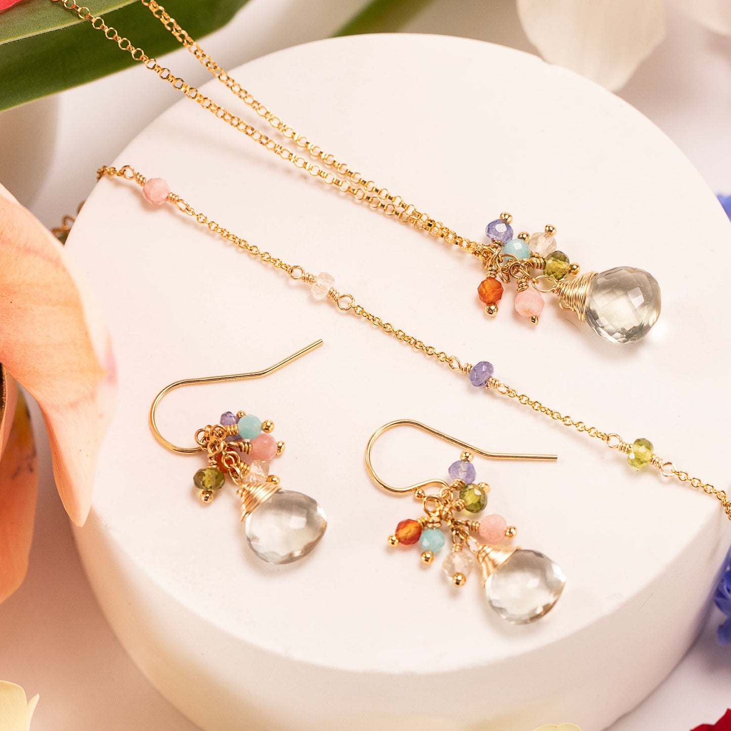 Jewelry set including necklaces and earrings on a white surface with flowers.