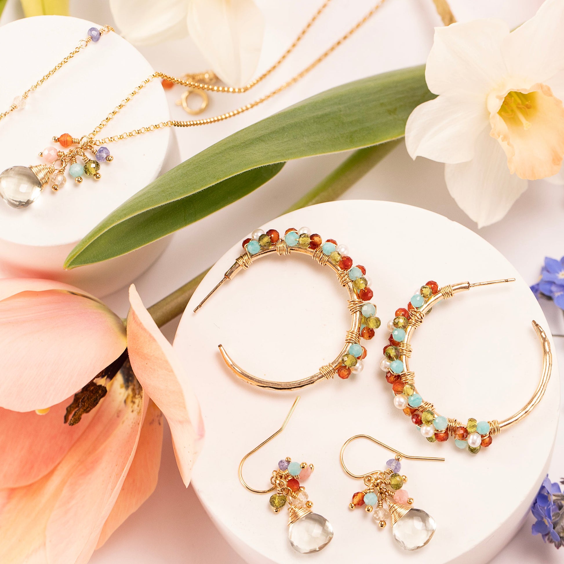 Jewelry set including earrings and necklaces on a white surface with flowers.